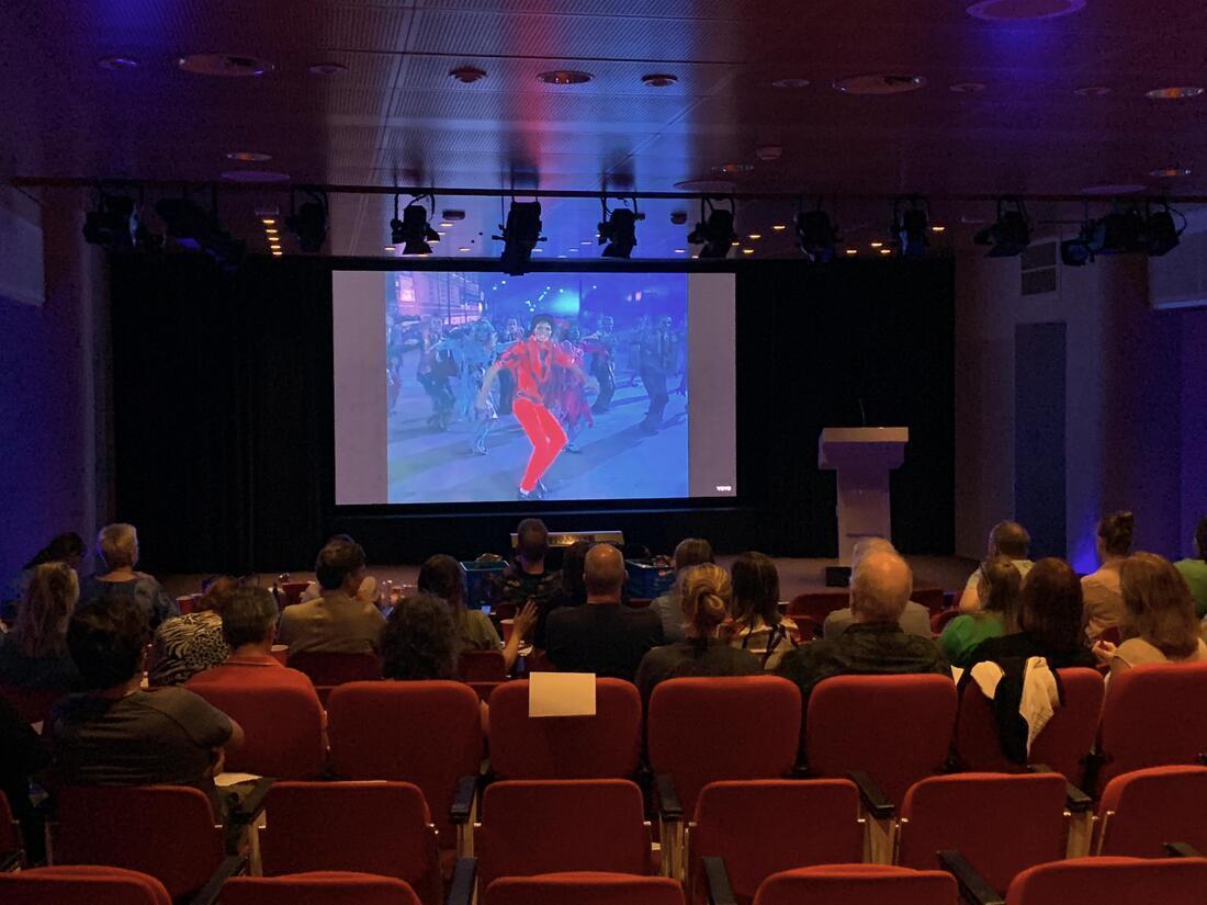 Mensen kijken in de aula van de KB naar videoclips