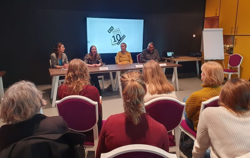 Vier mensen achter tafel, op de voorgrond publiek